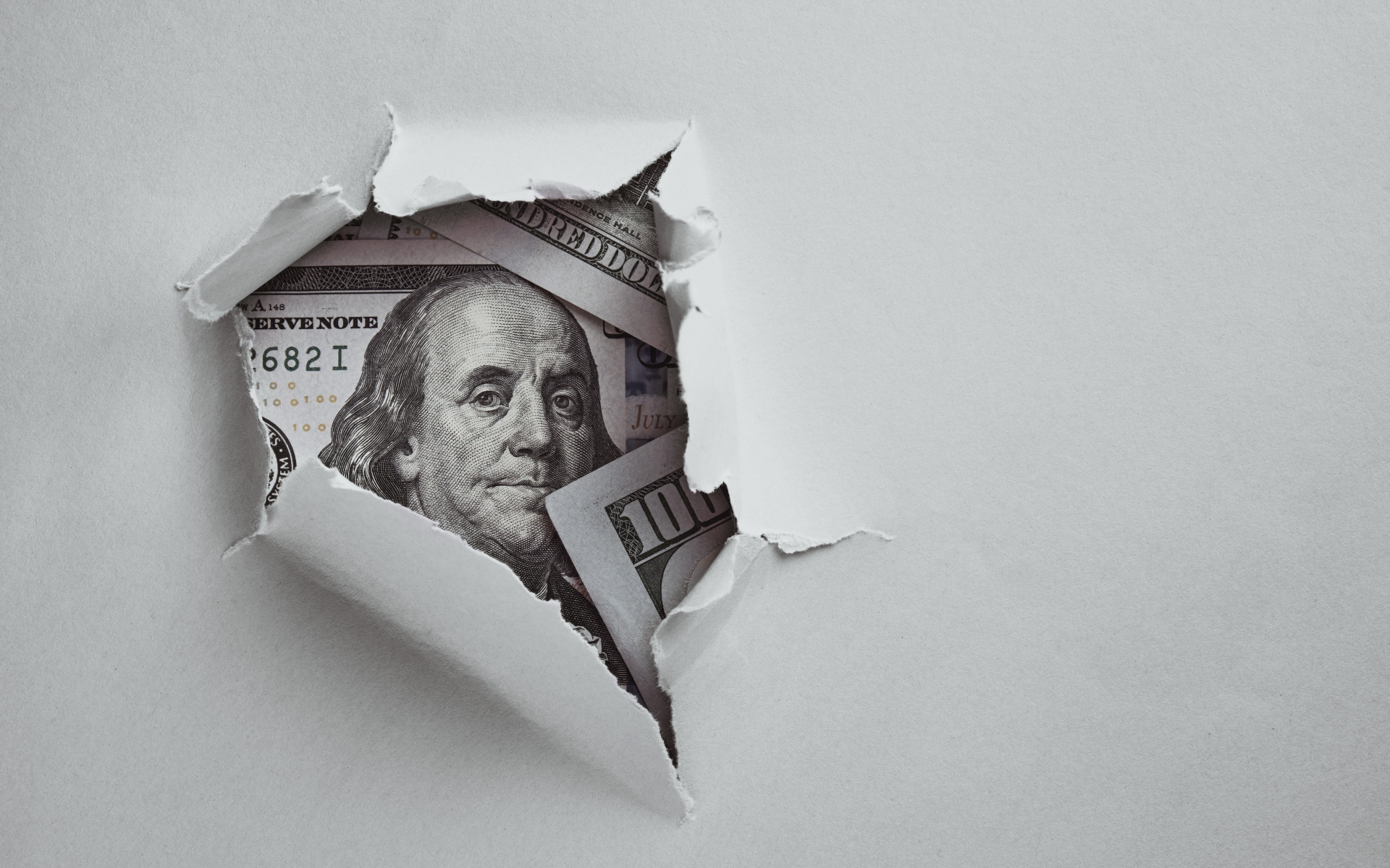 One-hundred-dollar bills exposed under torn sheet of paper