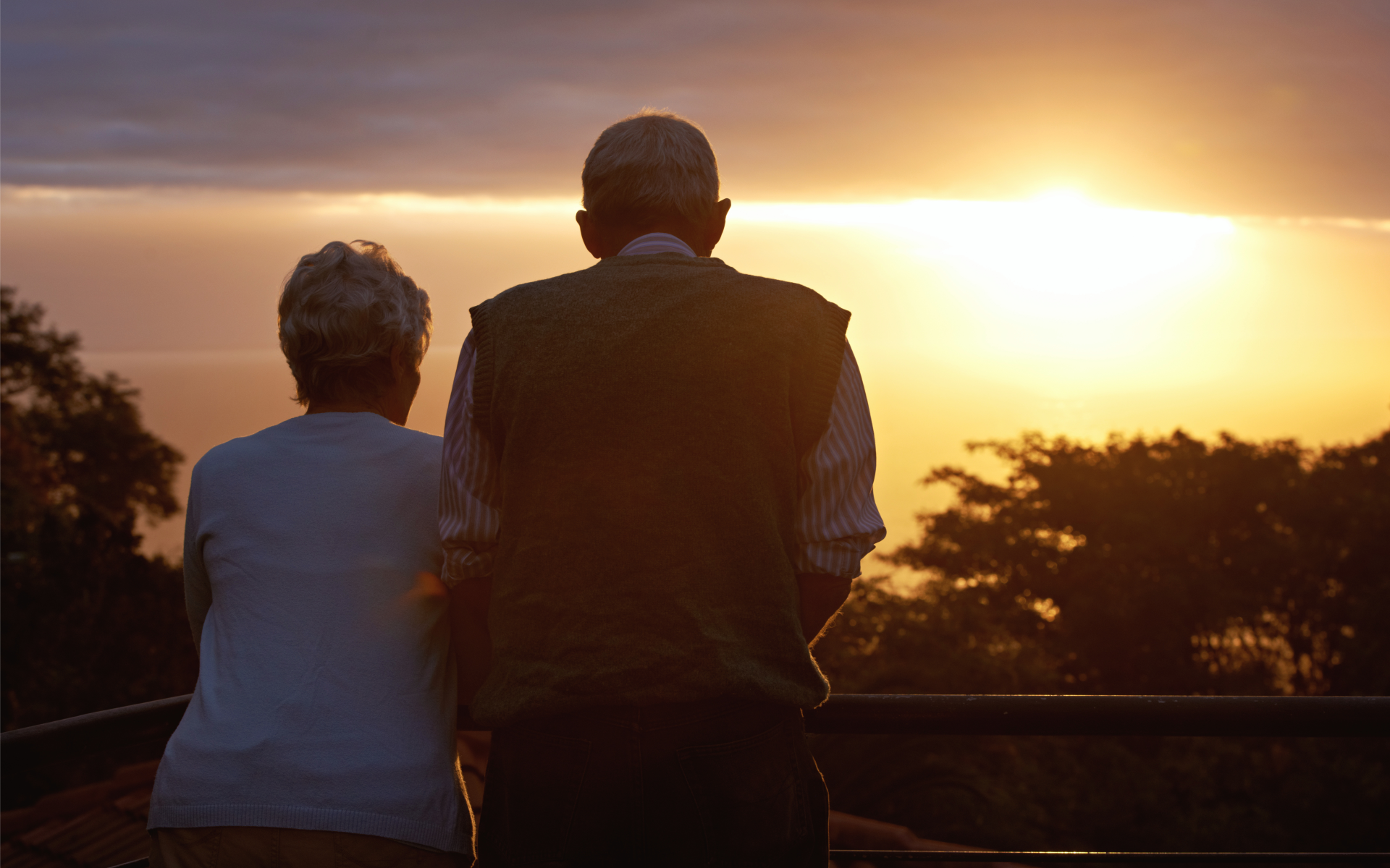 An elderly couple watches the sun set in retirement