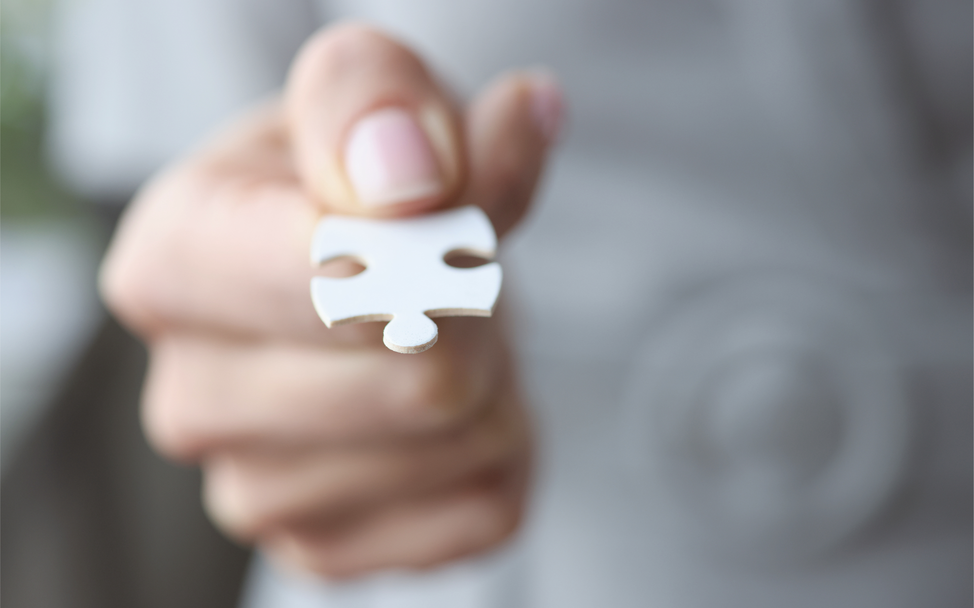 Fingers holding a single white puzzle piece