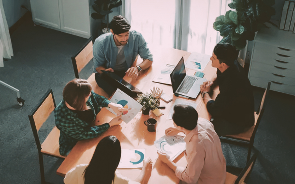 A group of colleagues sitting around a conference table, looking at documents and a laptop.
