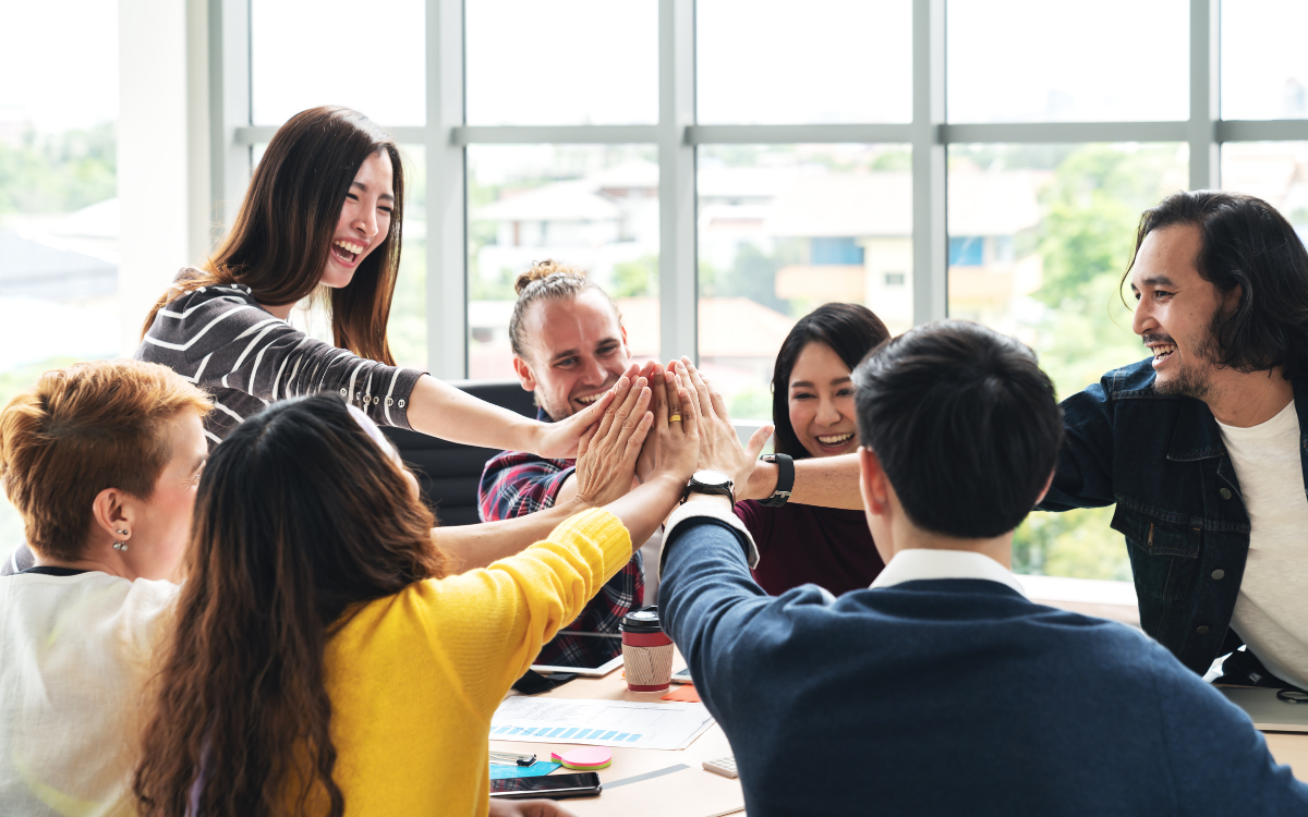 A group of colleagues high-fiving each other in a meeting room.